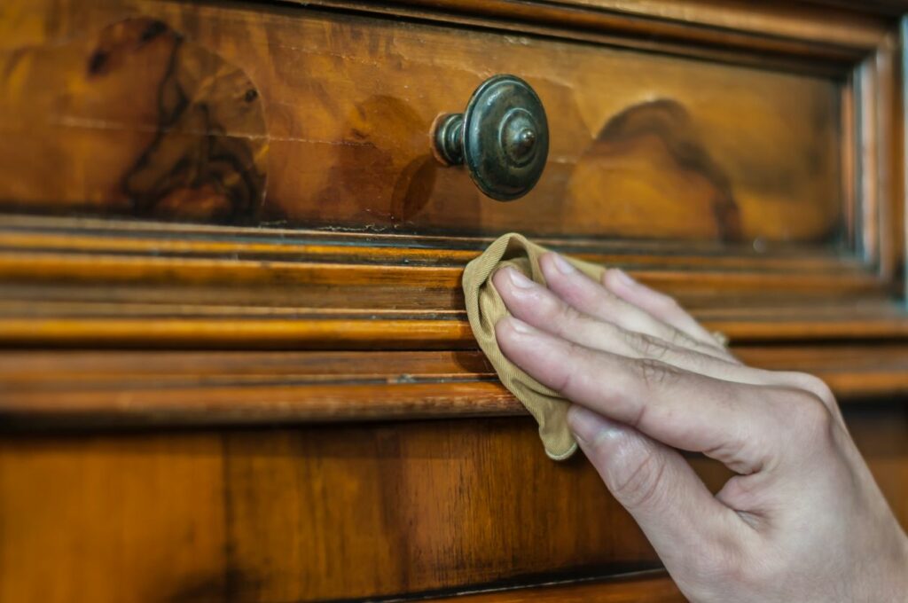 A person uses a small yellow-tan rag to polish the drawer on a wooden table.