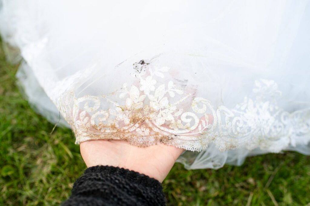 A person holds up the bottom of a wedding dress with the lace covered in dirt.