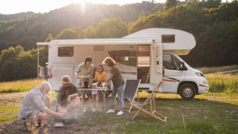 A family gathers outside of a camper at a folding table by a fire