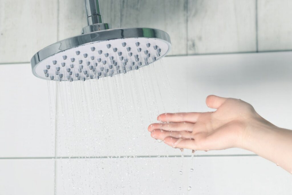 A person catches water falling from a showerhead.