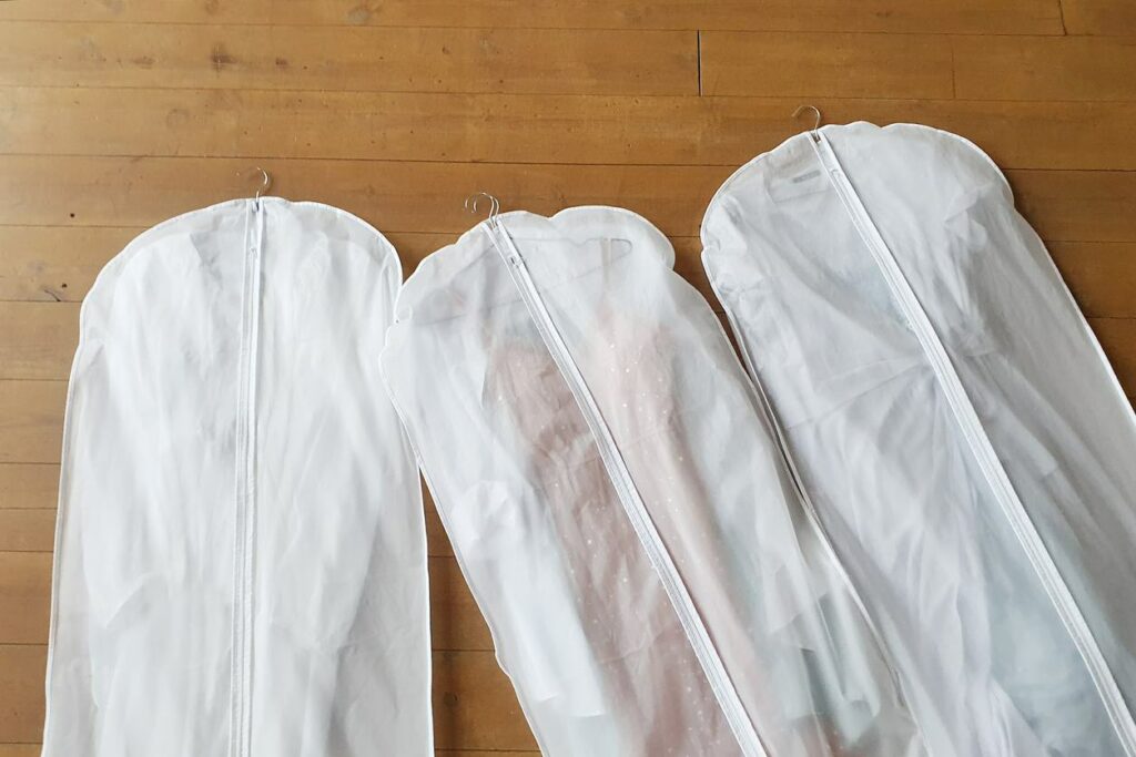 Three garment bags lay together on a wooden floor