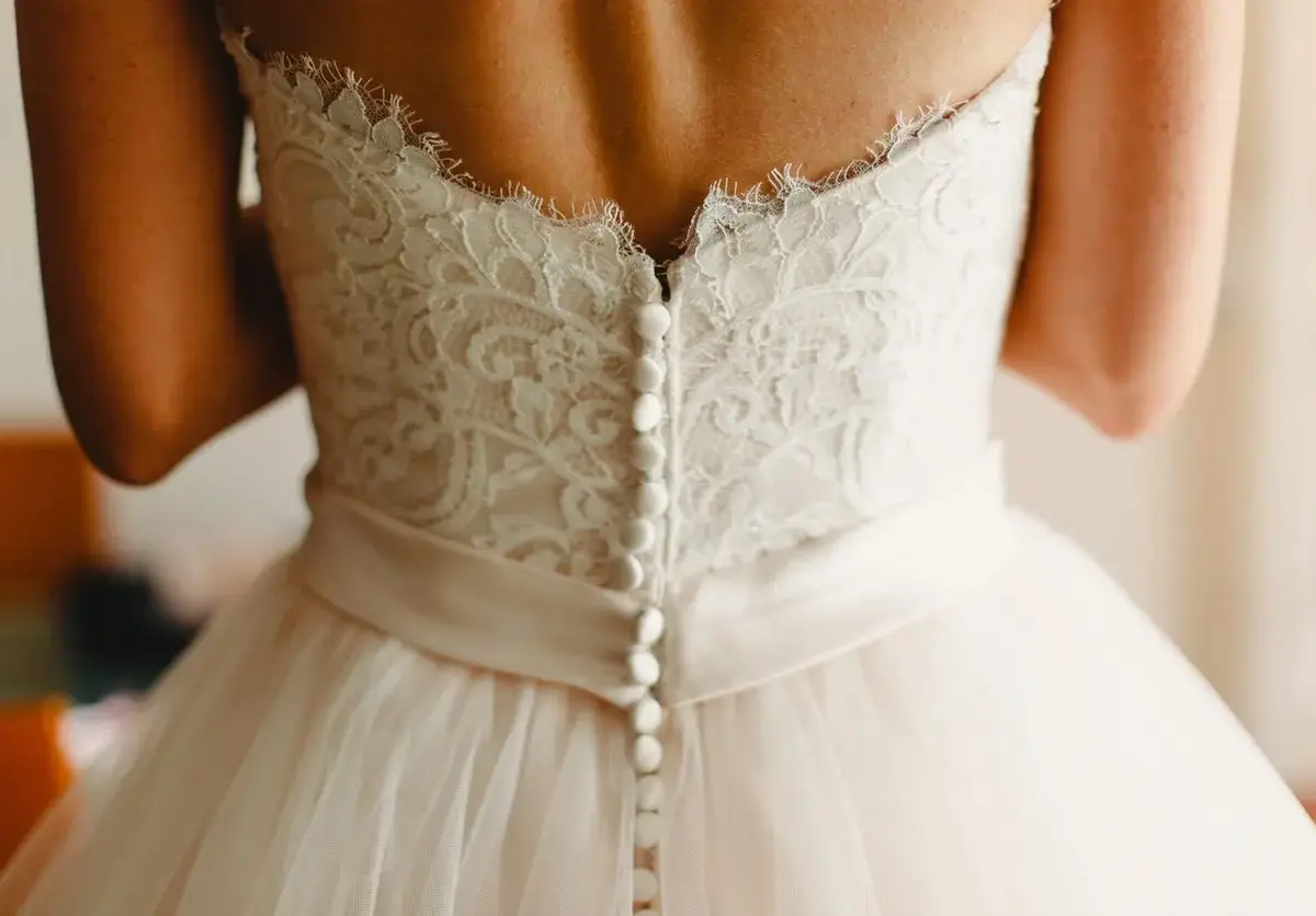 A woman is wearing a wedding dress with buttons up the back.