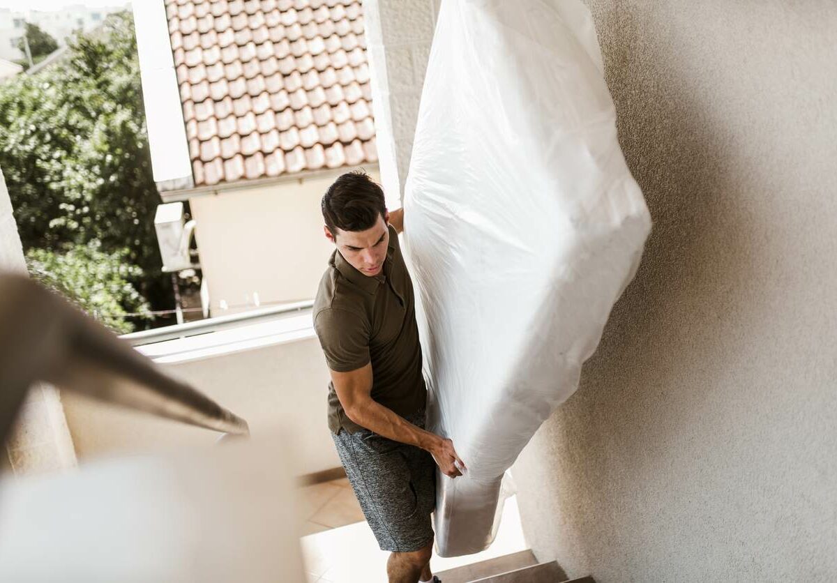 A man carries a mattress wrapped in plastic up a flight of stairs