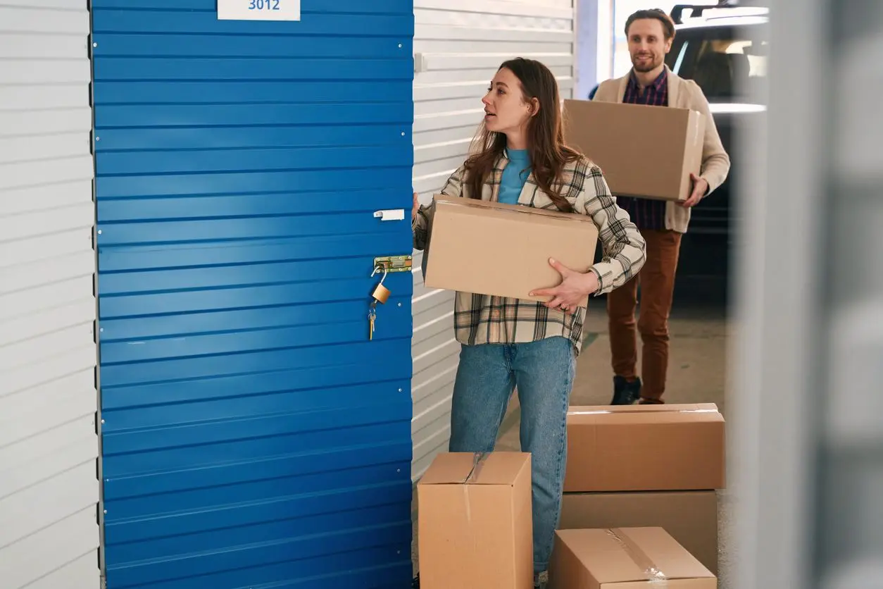 A woman and man carry cardboard boxes into their self storage unit.