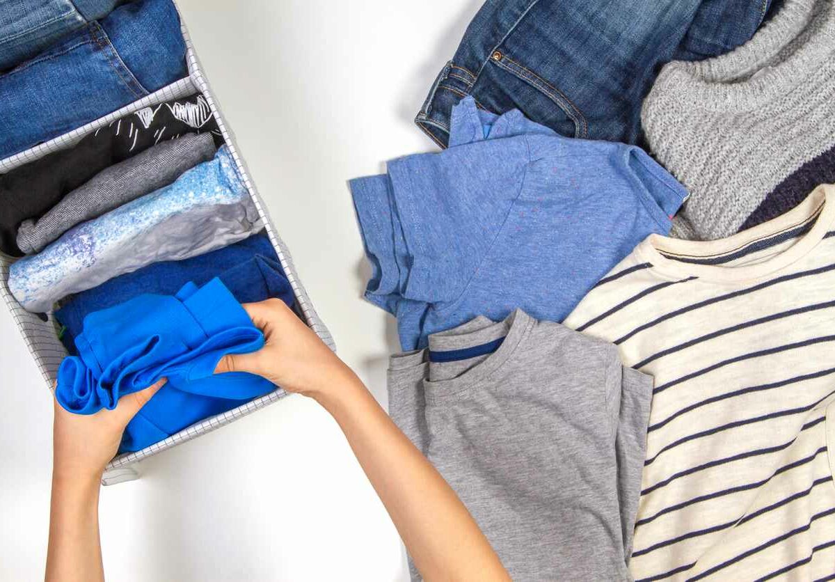 A person folds up pieces of clothing and puts them into a tub for storage.