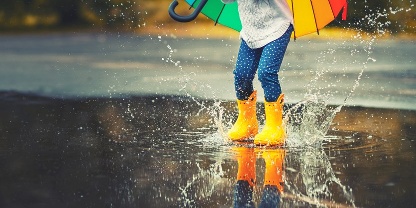 Feet of a child in yellow rubber boots jumping over a puddle in the rain