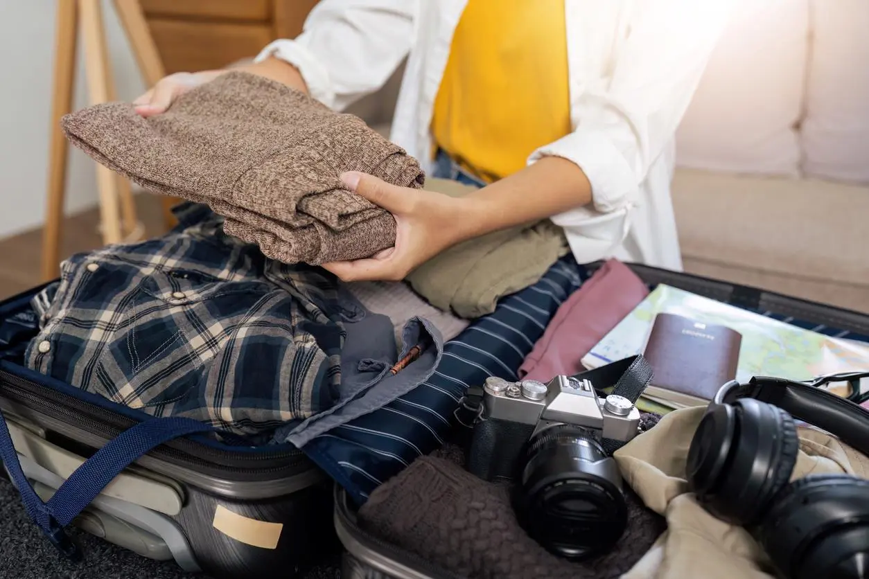 A person packing a suitcase with warm winter clothes.