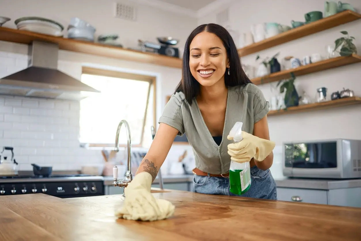 Happy young woman wiping off a kitchen table at home.