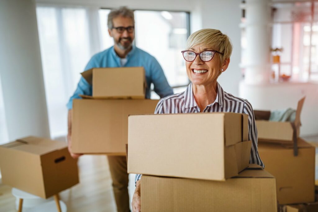 A portrait of a smiling senior couple holding cardboard boxes.