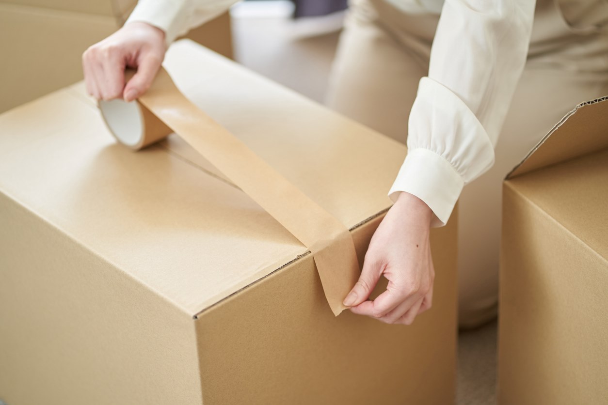 A woman sticks tape on cardboard boxes.