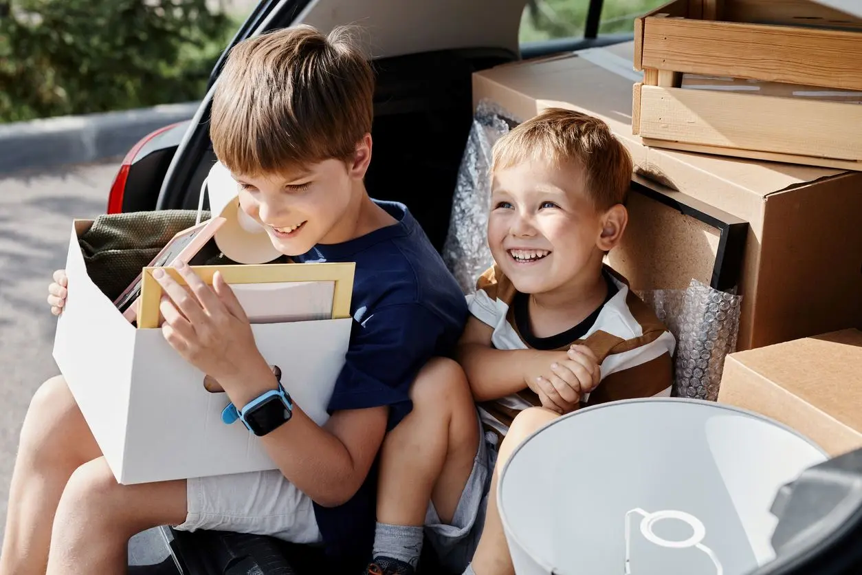 Two young kids smiling and sitting with cardboard boxes.