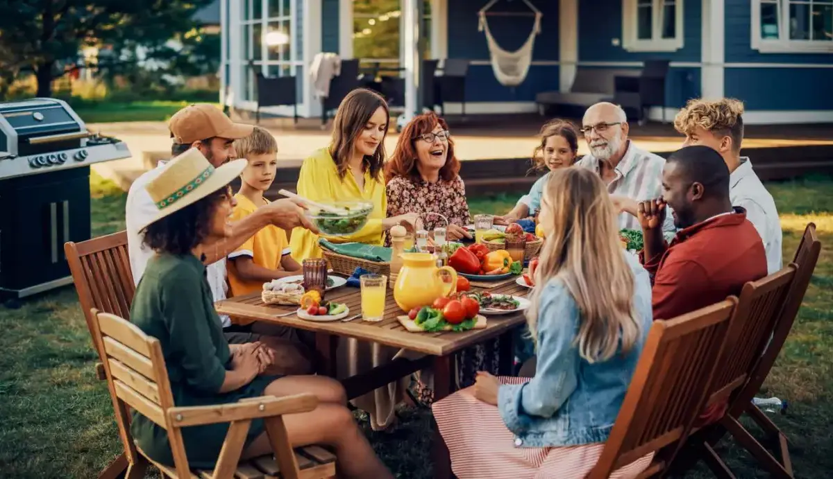 A joyful family having dinner at a backyard picnic table on a summer evening.