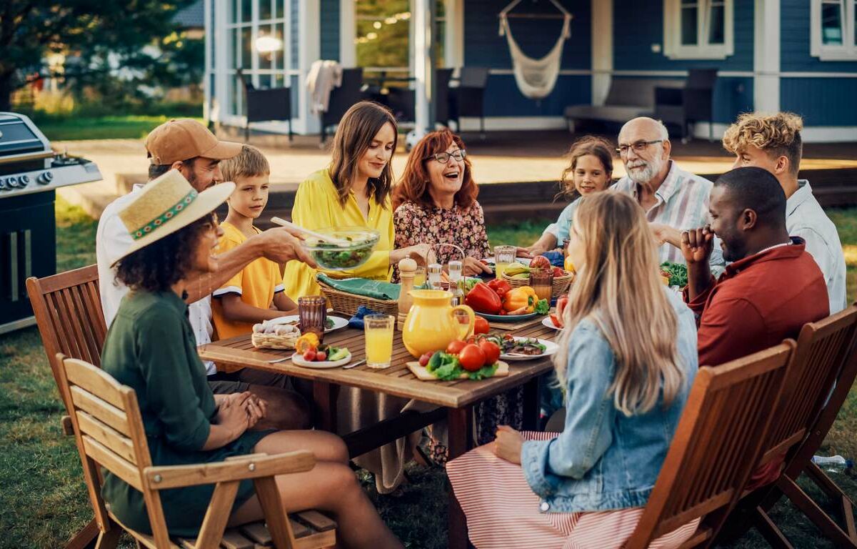 A joyful family having dinner at a backyard picnic table on a summer evening.