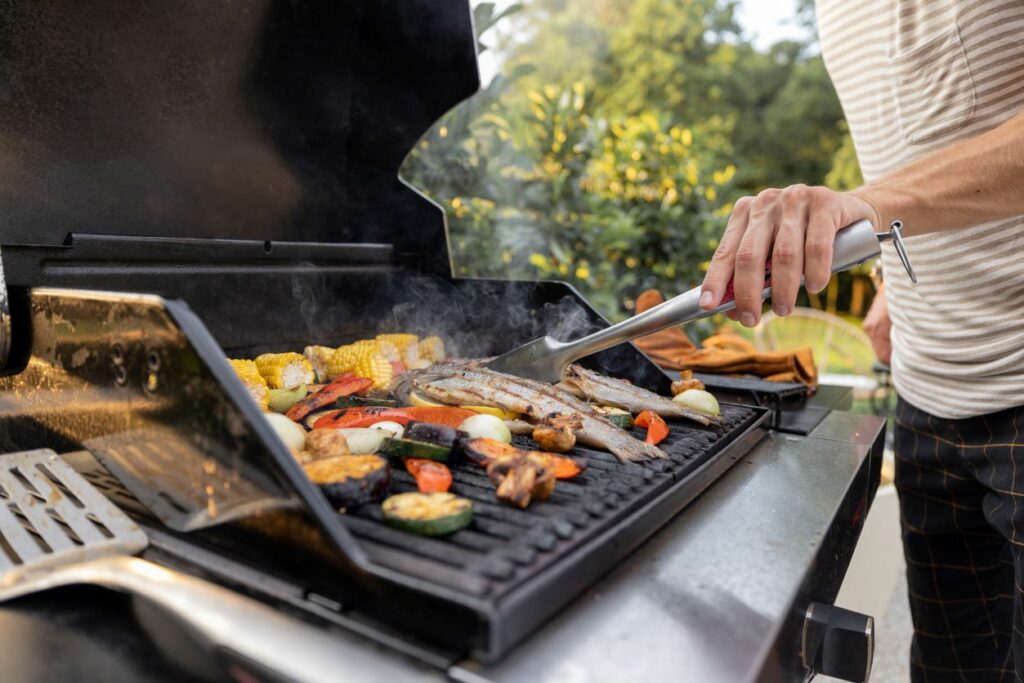 A man grilling fish and vegetables on a backyard grill during a summer day.