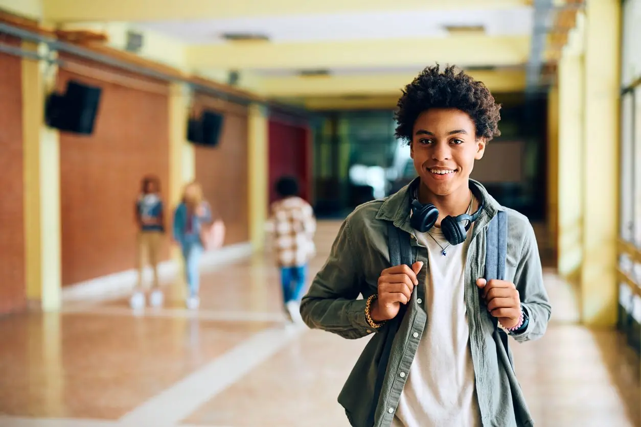 A male high school student wearing a backpack in the school hallway. 