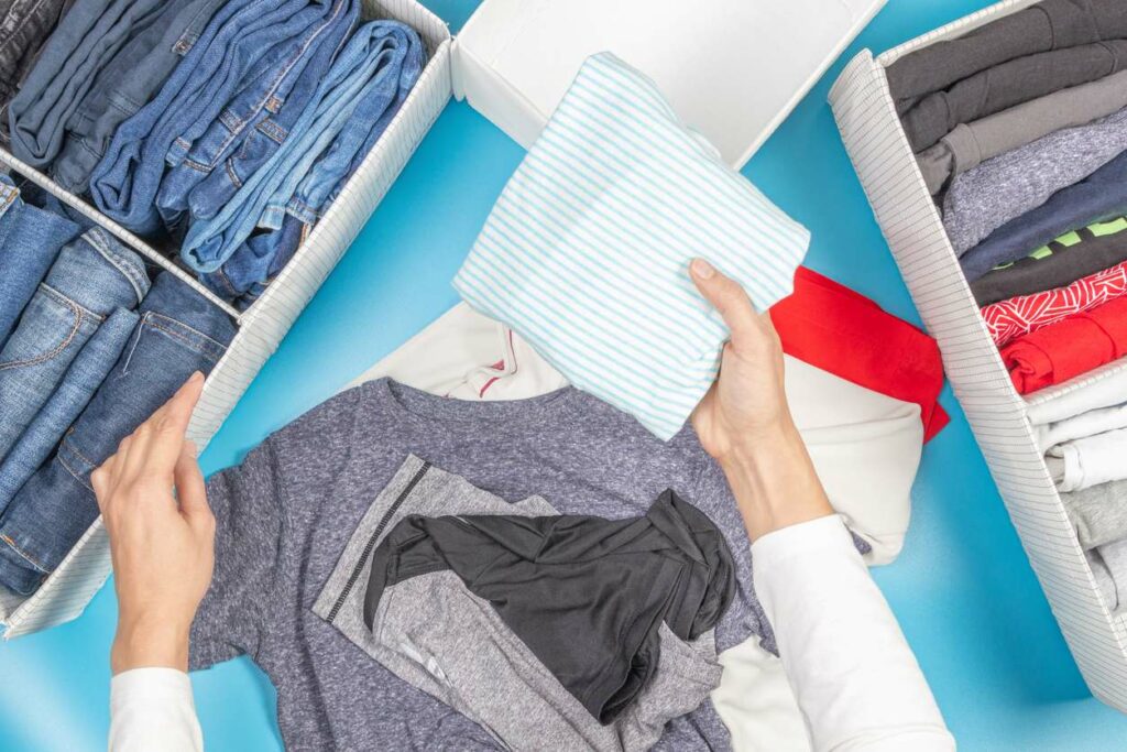 A person folds shirts and pants to place into organizers for storage purposes. 