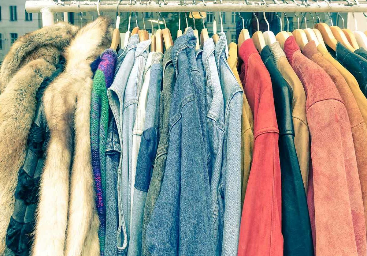 A clothing rack filled with vintage coats and jackets for sale at a flea market.