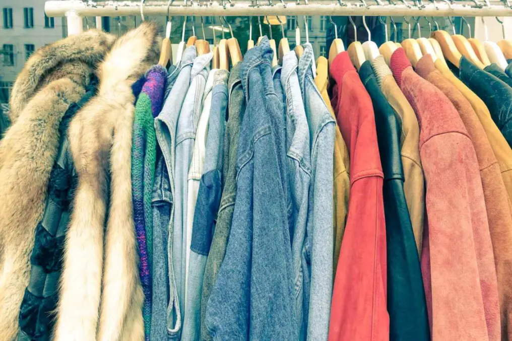 A clothing rack filled with vintage coats and jackets for sale at a flea market.