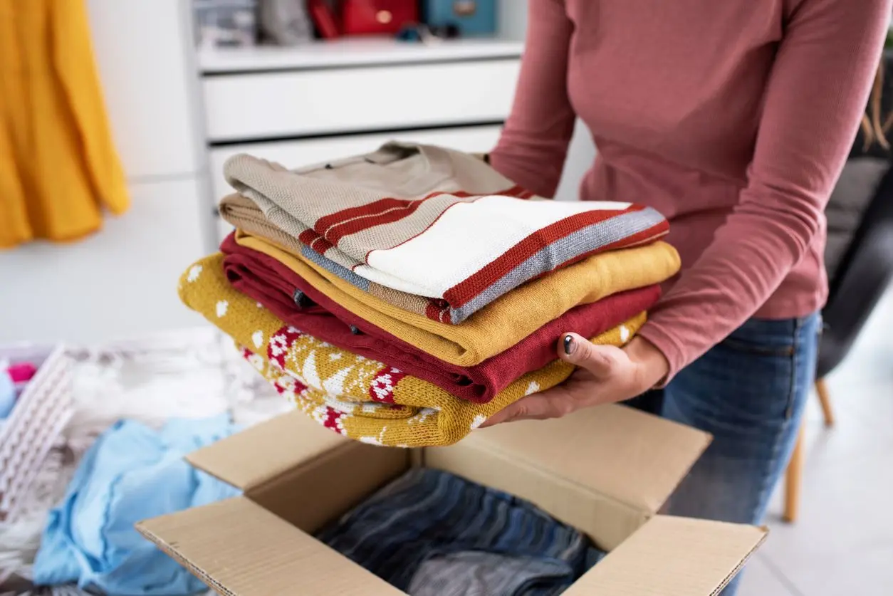 A woman places folded sweaters into a box for seasonal storage. 