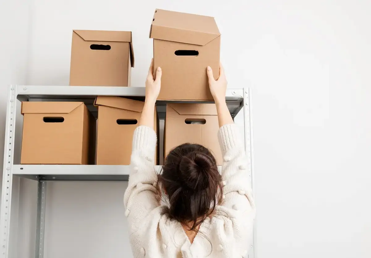 A woman puts a cardboard box on a shelf.