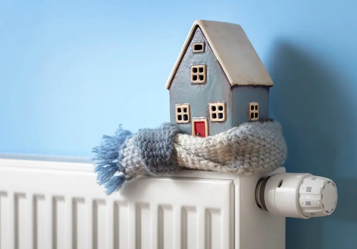 A blue miniature home sits on a radiator wrapped in a scarf.