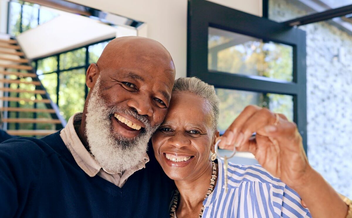 A senior couple smiles for the camera while the woman holds new house keys.