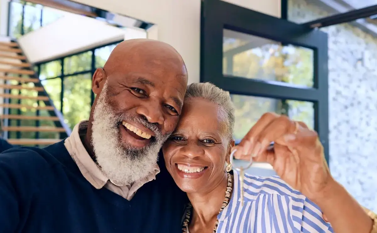 A senior couple smiles for the camera while the woman holds new house keys.