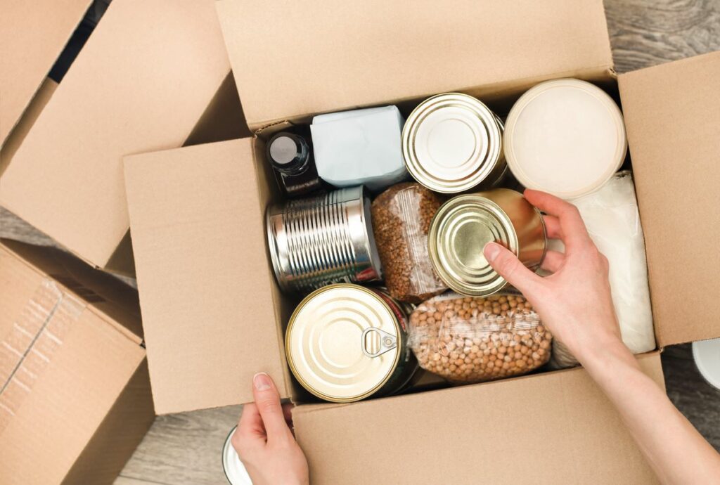 A person fills a cardboard box with nonperishable foods. 