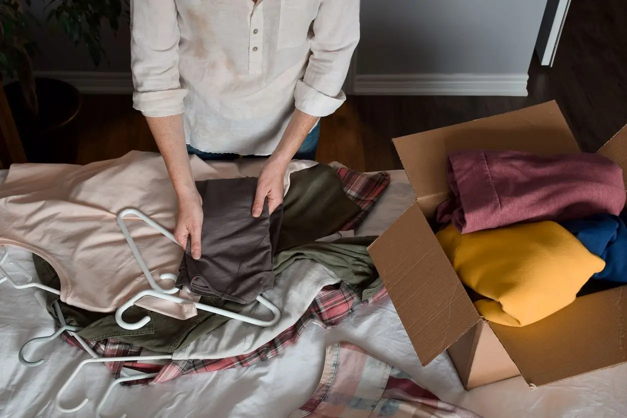 A person sorts through and folds clothing into a cardboard box. 