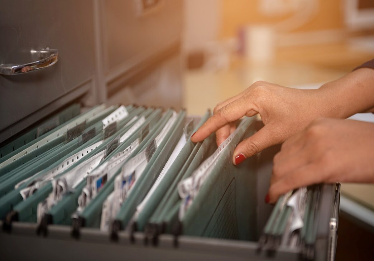 A person with red fingernails flips through the documents in a filing cabinet.