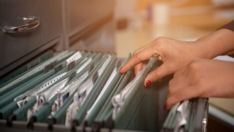 A person with red fingernails flips through the documents in a filing cabinet.