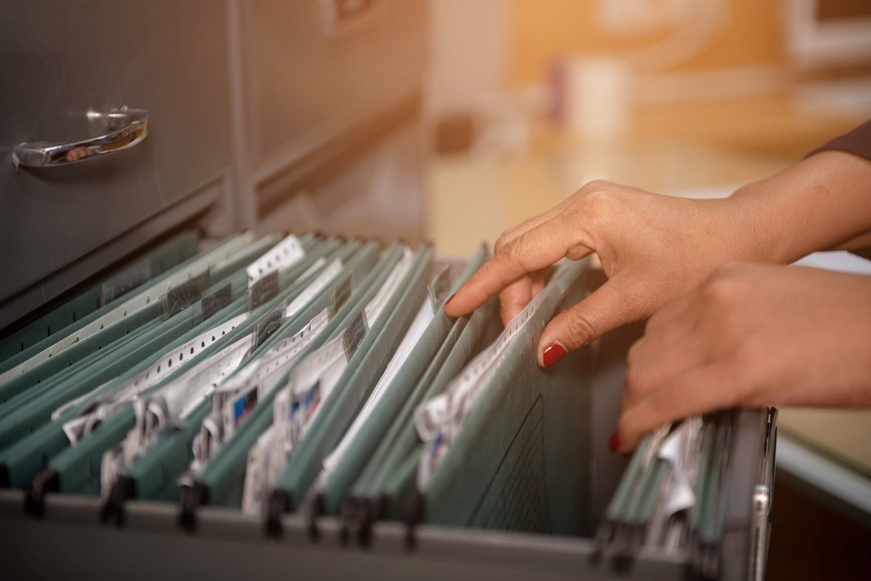A person with red fingernails flips through the documents in a filing cabinet.