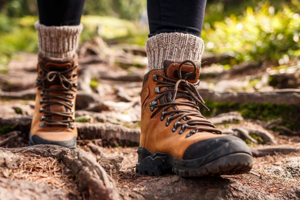 A person wearing sturdy brown hiking boots and thick, knitted socks walks a hiking trail. 