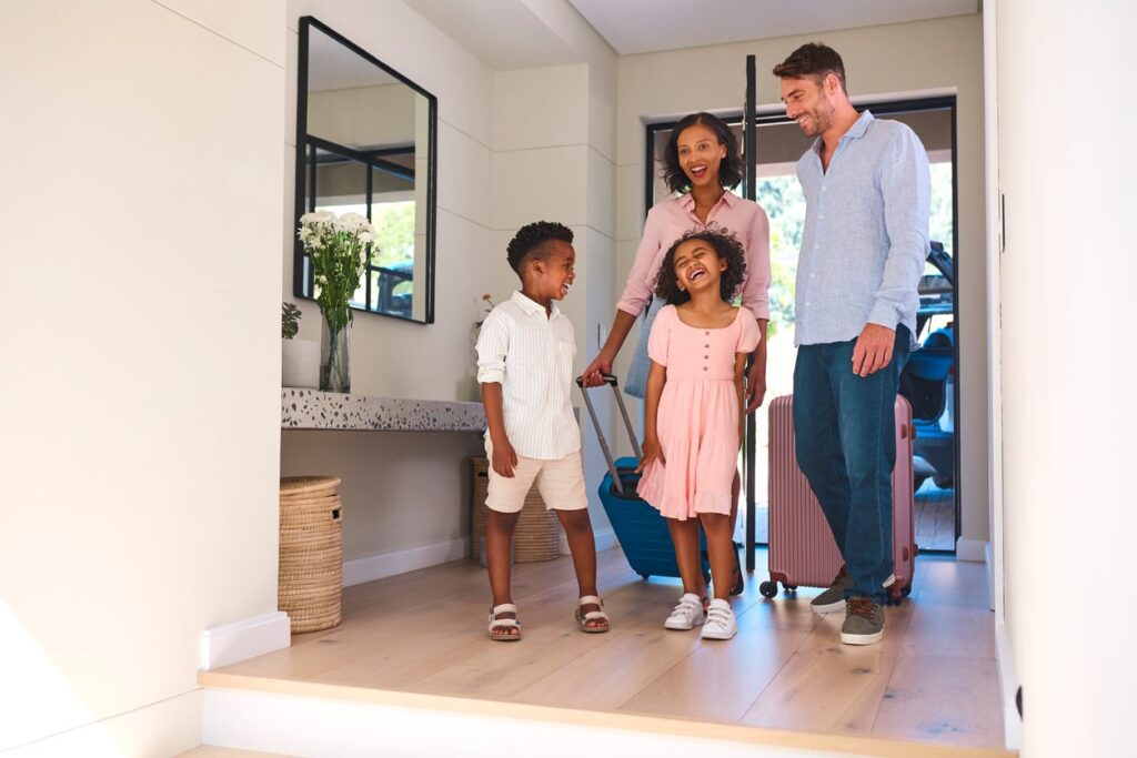 A smiling young family walks into their rental property for vacation.