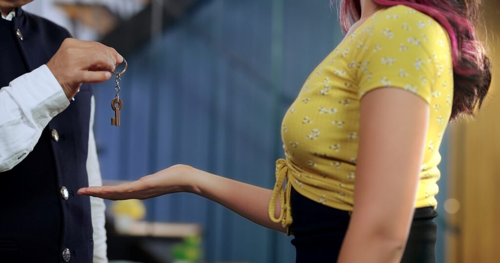 A landlord in a vest gives a woman in yellow a pair of apartment keys. 