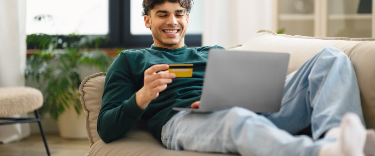 A young man lounging on a couch paying for an online purchase with a credit card.