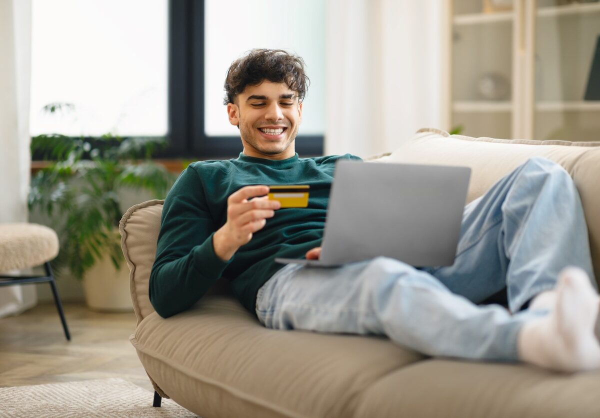 A young man lounging on a couch paying for an online purchase with a credit card.