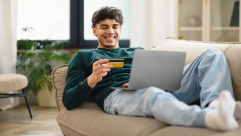 A young man lounging on a couch paying for an online purchase with a credit card.