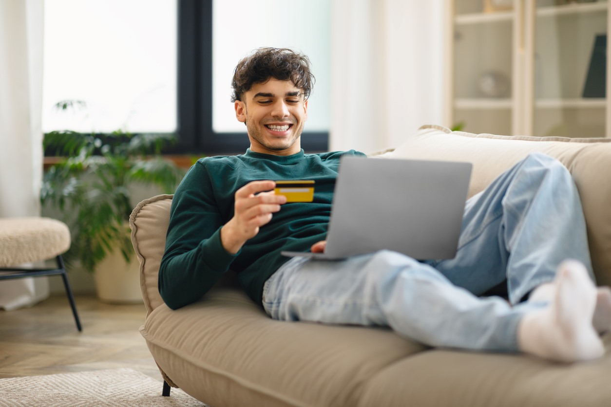A young man lounging on a couch paying for an online purchase with a credit card.