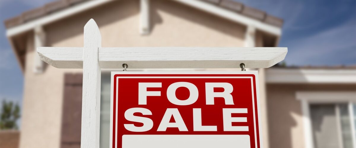 A red and white for sale sign in front of a house.