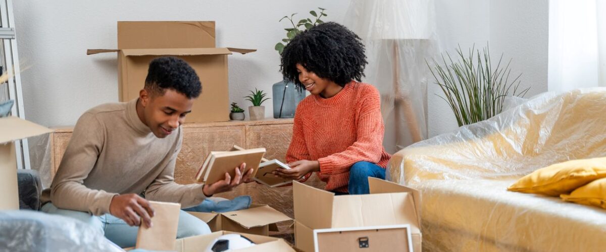 A smiling young couple unpacks moving boxes in the living room of their new home.