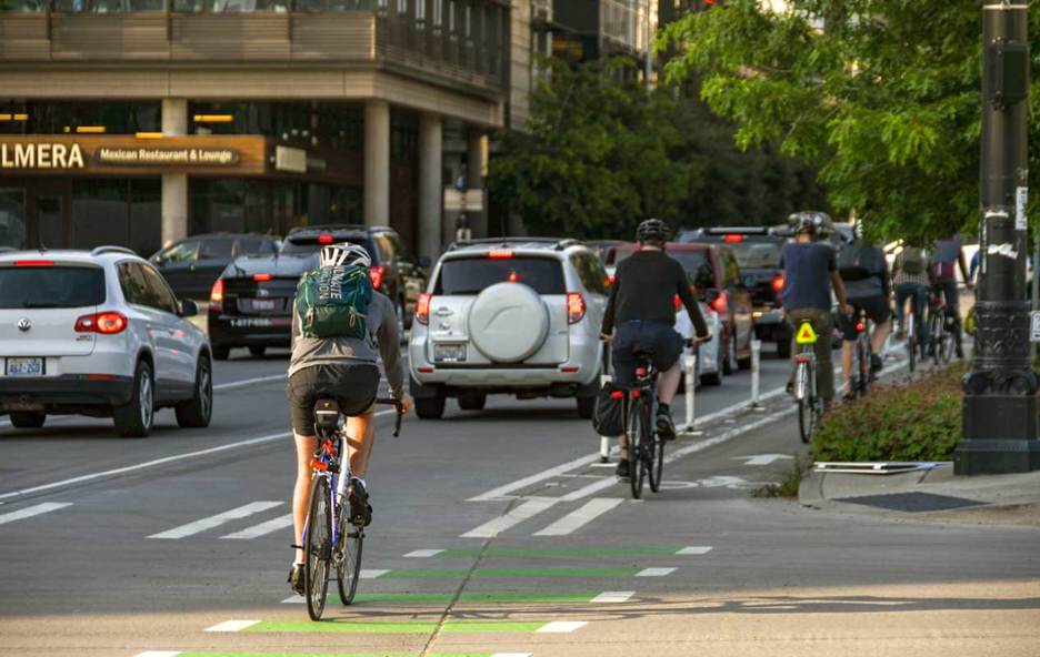 A Seattle street is filled with traffic from cars and cyclists on a sunny day. 