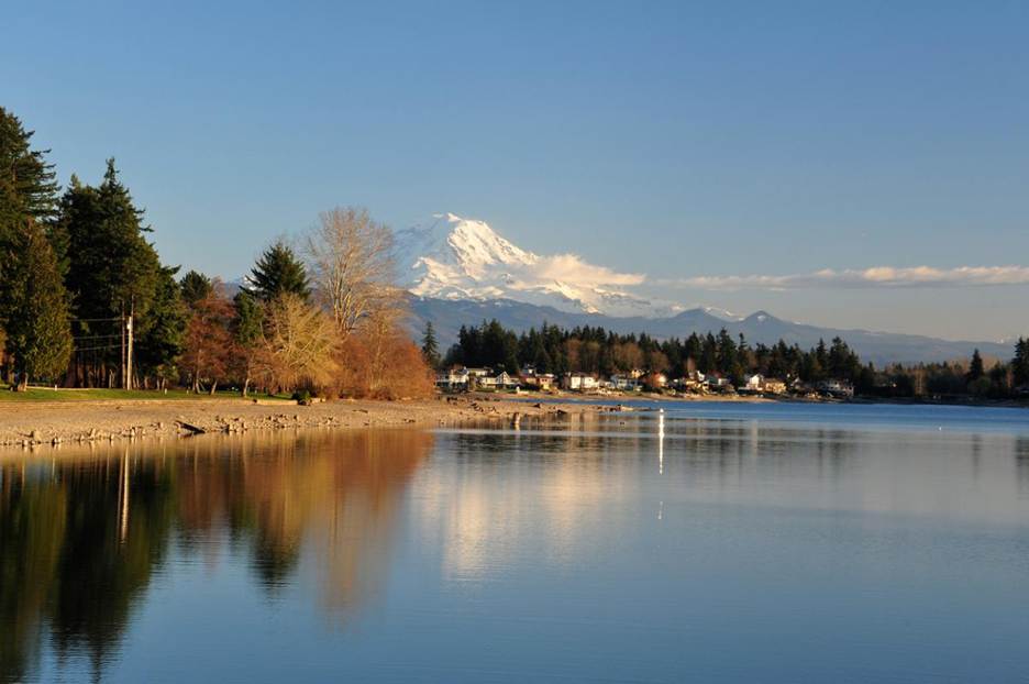 The sun begins to set on Lake Tapps with water reflecting the trees, and Mount Rainier stands in the distance.