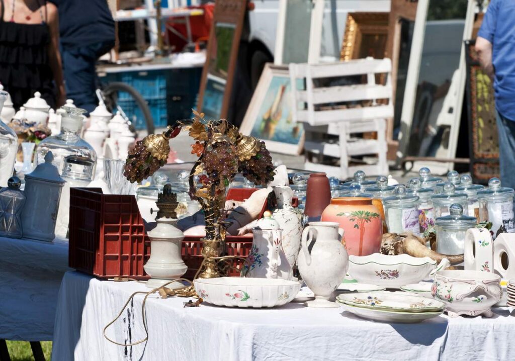 A table filled with vintage lamps, dishes, and glassware on display at an outdoor garage sale.
