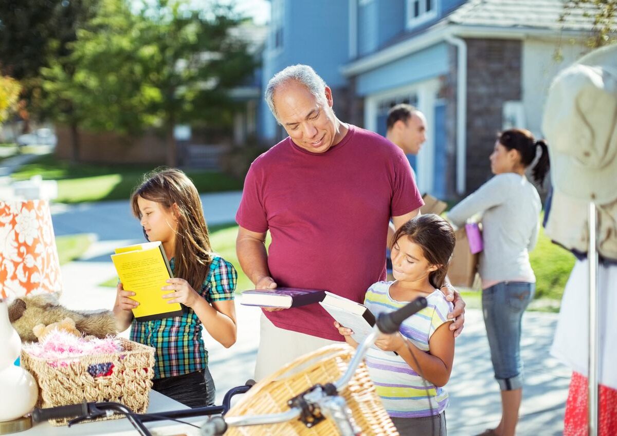 A grandfather and his two granddaughters browse books at a neighborhood garage sale.