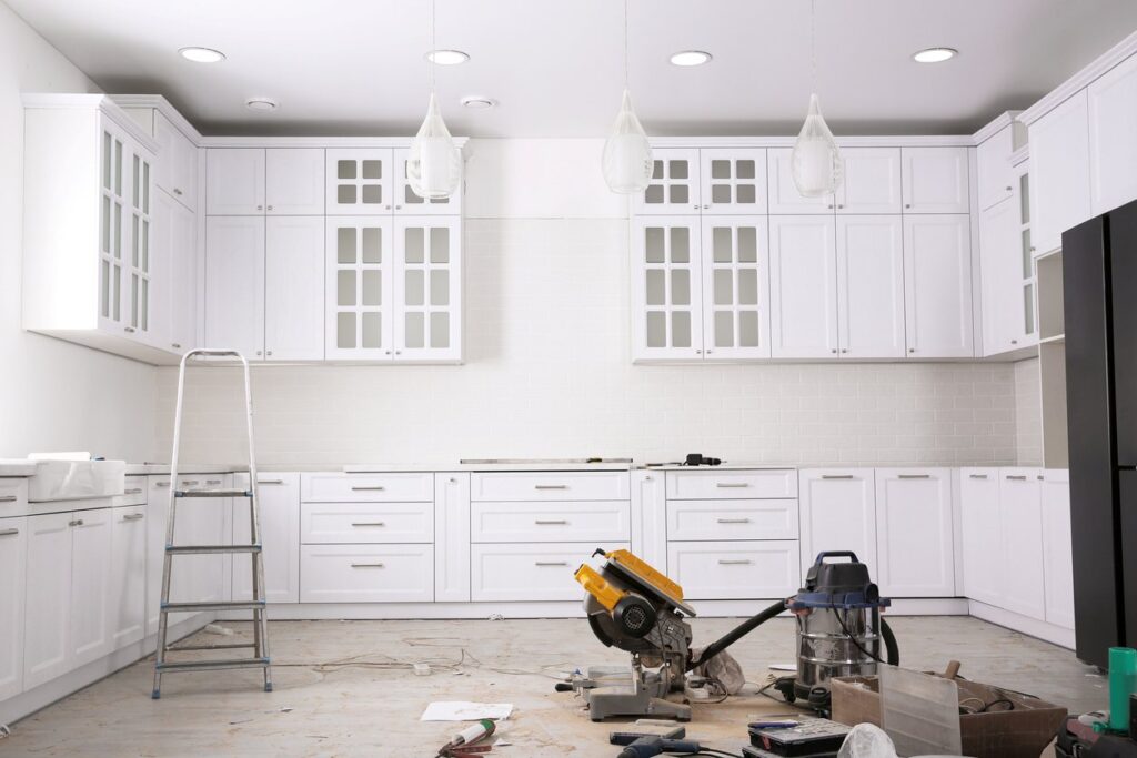 A white kitchen in the process of being remodeled with construction tools on the right, and a ladder. 