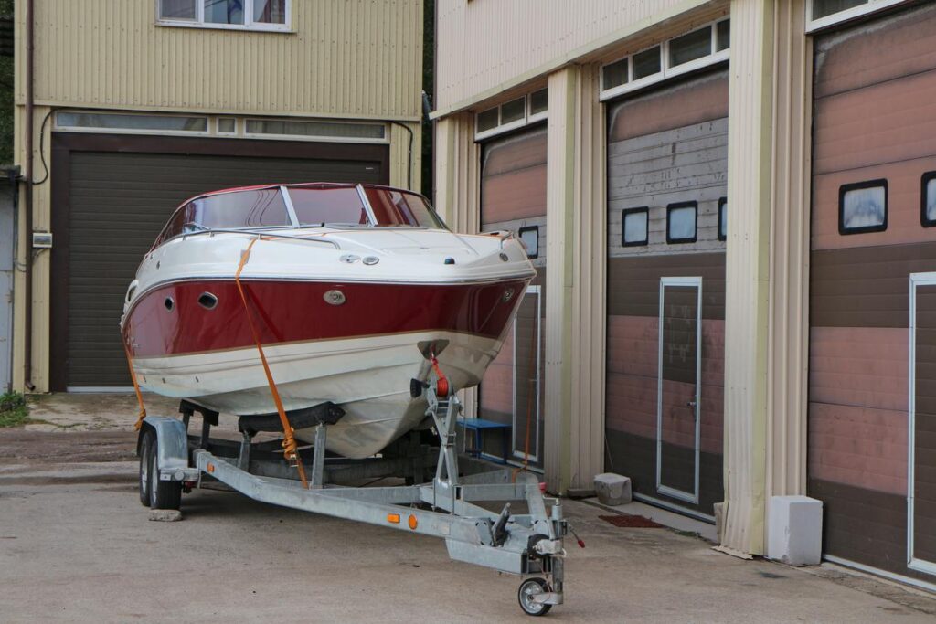 A white boat with a red stripe on a trailer about to be parked in an indoor storage unit. 