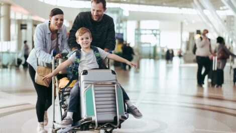 Parents pushing a luggage cart with their child through an airport terminal.