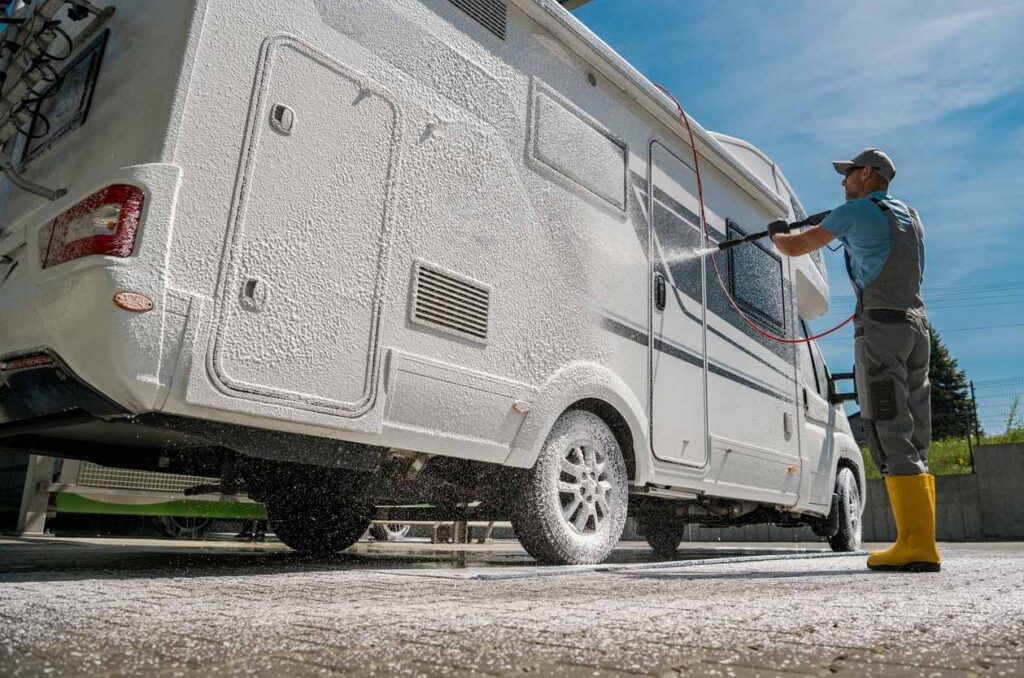 Person washing a motorhome exterior with foam soap.